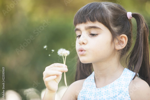 Cute little girl blowing dandelion flower outdoors. Carefree childhood concept