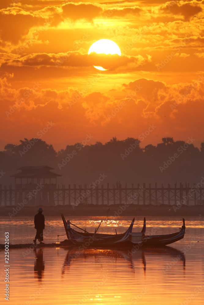 Silhouette of oarsman on boat with broad lake at during sunrise, U-Bein bridge, Mandalay, Myanmar