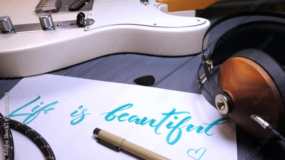 Life is beautiful text. Font of lettering word on white paper with green ink by calligrapher. Music frame - guitar, headphones. Graphic design, lettering, concept. 4k. Life is beautiful text. Font of lettering word on white paper with green ink by calligrapher. Music frame - guitar, headphones. Graphic design, lettering, concept. 4k.