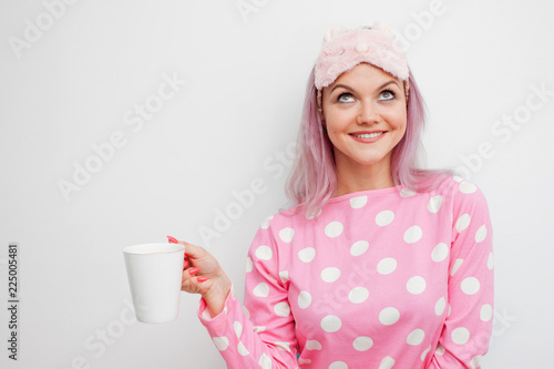 Happy young woman drink morning coffee. Beautiful girl in pink pajamas and sleepmask