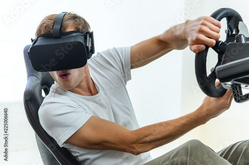 A young, handsome guy in a white T-shirt, playing in a race, on a simulator of virtual reality