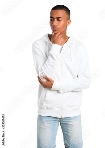 Dark-skinned young man with white sweatshirt standing and looking to the side with the hand on the chin on isolated white background © luismolinero