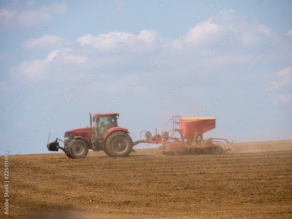 Fototapeta premium Tractor with a modern sowing seeds machine in a newly plowed field. Plowed land as a background. Red tractor on the field.