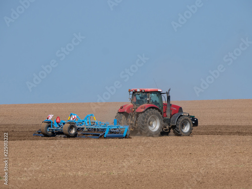 Red tractor with plow on the field. Tractor on the field. Summer field and red tractor.