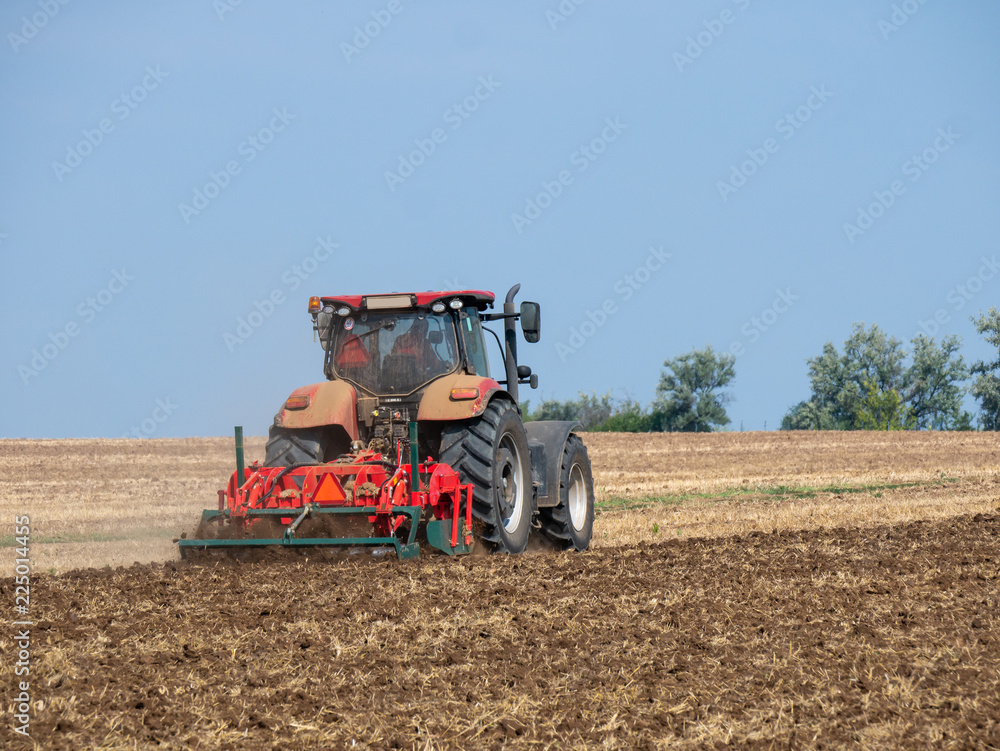Fototapeta premium Red tractor with plow on the field. Tractor on the field. Summer field and red tractor.