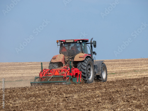 Red tractor with plow on the field. Tractor on the field. Summer field and red tractor.