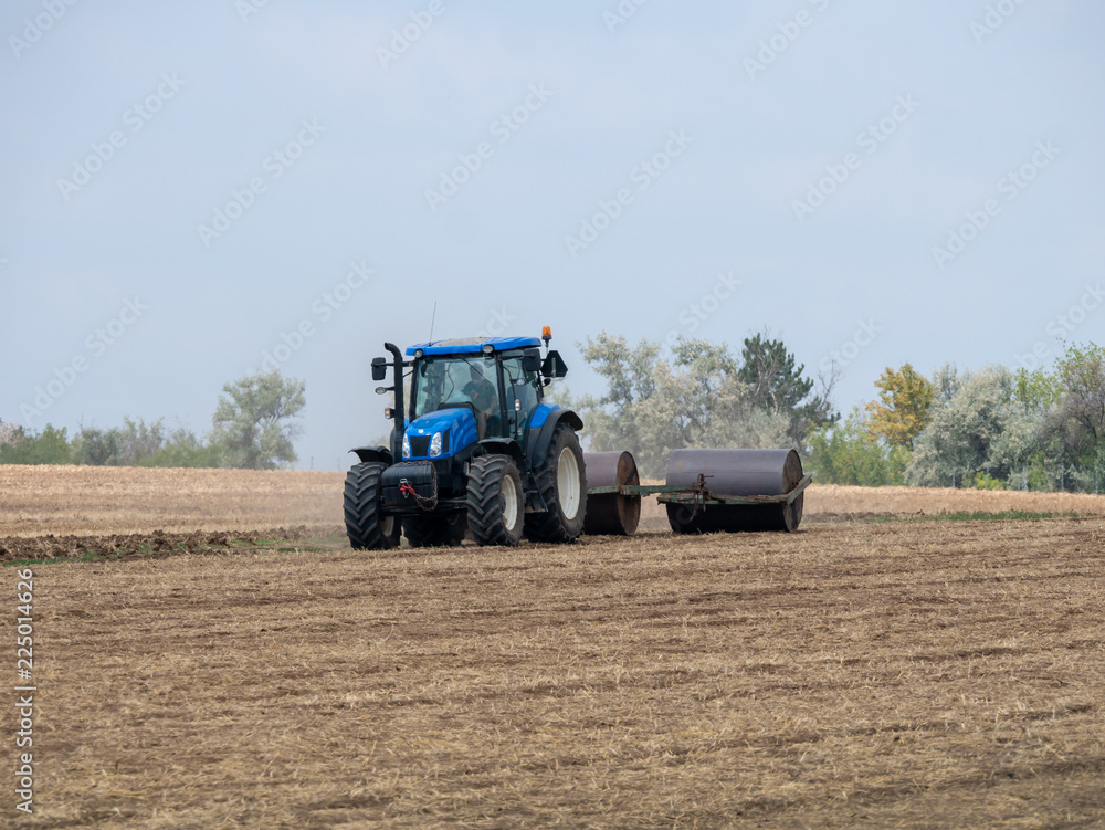Tractor pulls rollers on the field. Blue Tractor with rollers on the field. Tractor on summer field. Tractor pulls rollers on the field. Blue Tractor with rollers on the field. Tractor on summer field.