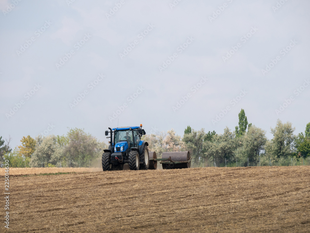 Tractor pulls rollers on the field. Blue Tractor with rollers on the field. Tractor on summer field. Tractor pulls rollers on the field. Blue Tractor with rollers on the field. Tractor on summer field.