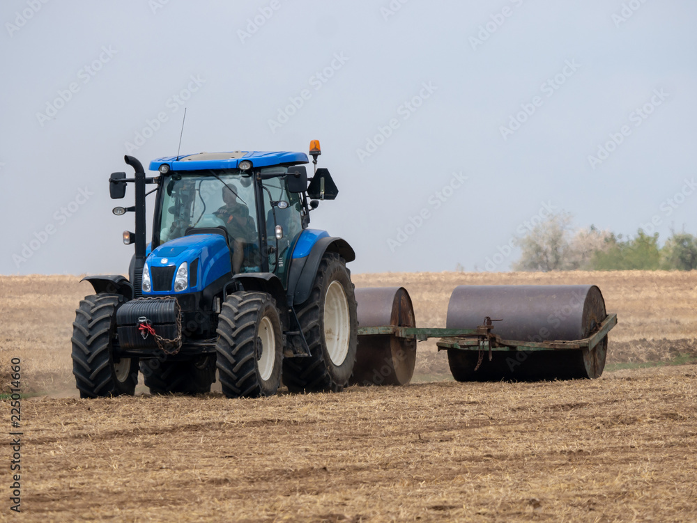 Fototapeta premium Tractor pulls rollers on the field. Blue Tractor with rollers on the field. Tractor on summer field.