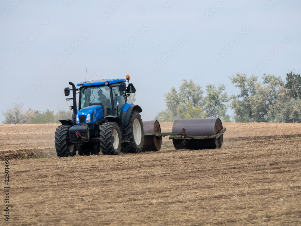 Tractor pulls rollers on the field. Blue Tractor with rollers on the field. Tractor on summer field. Tractor pulls rollers on the field. Blue Tractor with rollers on the field. Tractor on summer field.