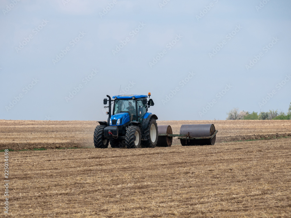 Tractor pulls rollers on the field. Blue Tractor with rollers on the field. Tractor on summer field. Tractor pulls rollers on the field. Blue Tractor with rollers on the field. Tractor on summer field.