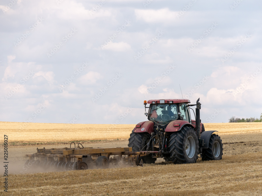Obraz premium Red tractor with plow on harvest field. Summer field and red tractor. Tractor on harvest field. Lowing after harvest. Plowing on the field.