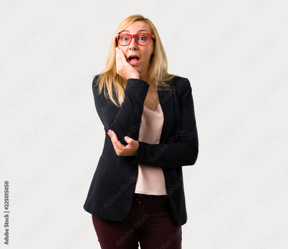 Middle-age blonde business woman with black jacket surprised and shocked while looking right. Expressive facial emotion on isolated grey background Middle-age blonde business woman with black jacket surprised and shocked while looking right. Expressive facial emotion on isolated grey background