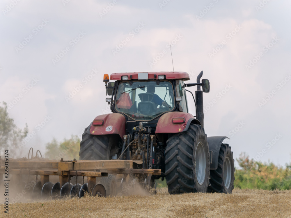 Obraz premium Red tractor with plow on harvest field. Summer field and red tractor. Tractor on harvest field. Lowing after harvest. Plowing on the field.
