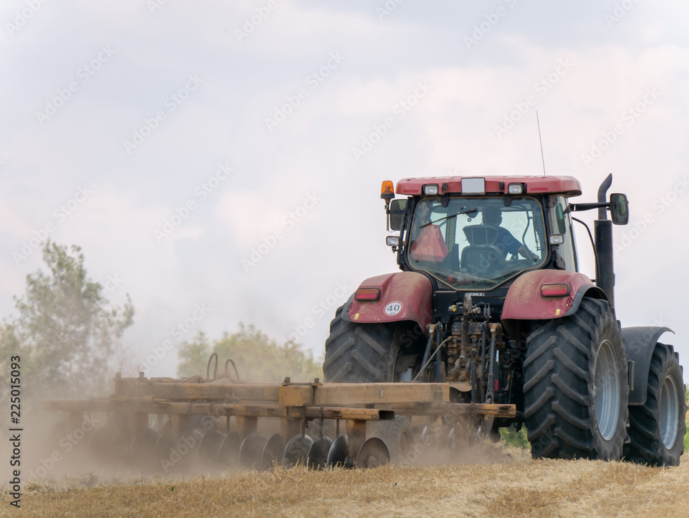 Fototapeta premium Red tractor with plow on harvest field. Summer field and red tractor. Tractor on harvest field. Lowing after harvest. Plowing on the field.
