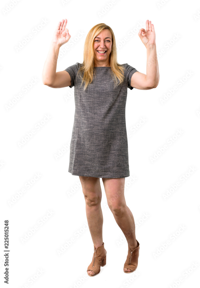 Middle age blonde woman with grey dress showing an ok sign with fingers. Face of happiness and satisfaction on isolated white background Middle age blonde woman with grey dress showing an ok sign with fingers. Face of happiness and satisfaction on isolated white background