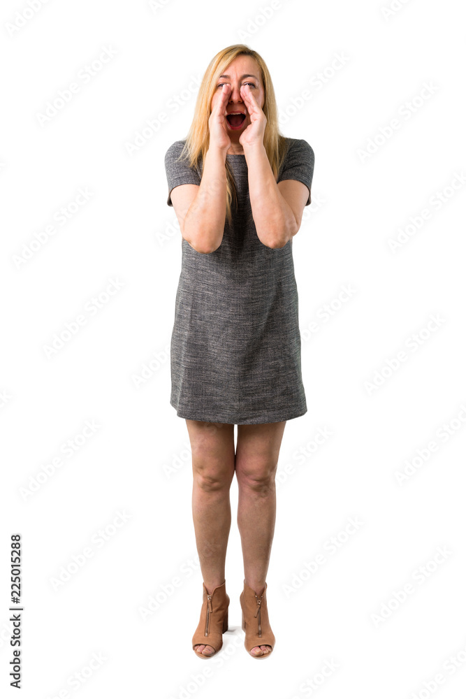 Fototapeta premium Middle age blonde woman with grey dress shouting with mouth wide open to the lateral and announcing something on isolated white background
