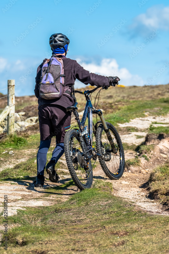 Obraz premium Sportsman is pushing his bike up on the mountain path