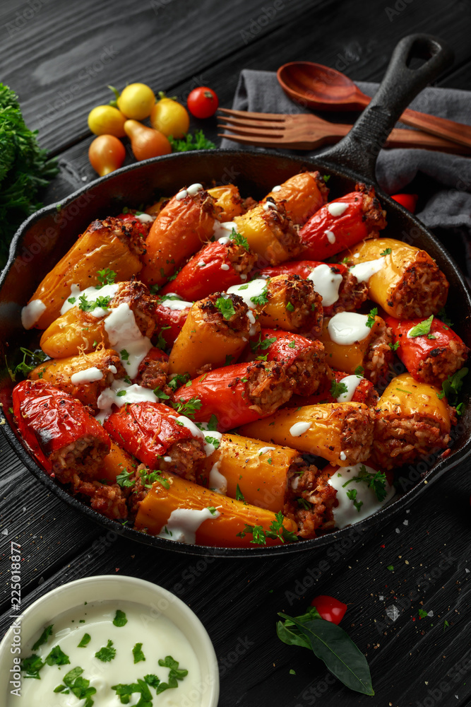 Sausage meat, mince and rice Stuffed sweet mini bell peppers baked in cast iron skillet, pan topped with yogurt and fresh parsley