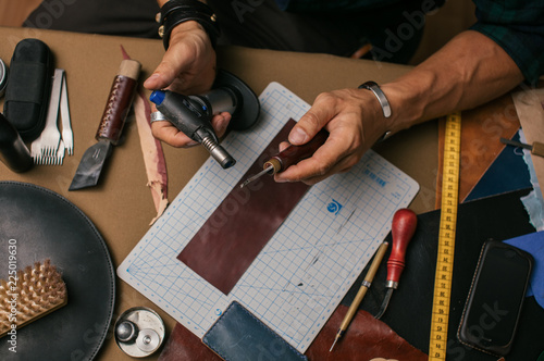 Skilled professional shoemaker making custom made leather wallet from genuine leather samples at a workshop, close up high angle shot.