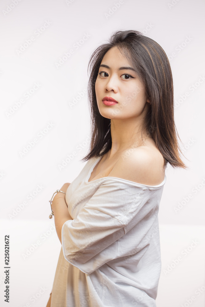 Close up studio shot of calm Asian young woman with healthy clean skin,  gorgeous dark hair and expressive big eyes in white t-shirt looking at  camera with calm and serious expression. foto