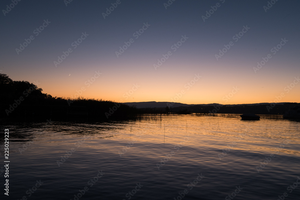 Sunset in Switzerland, view of the Lake Murten, moon rising and sun setting