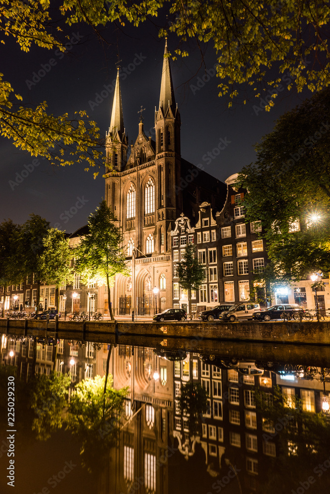 Catholic cathedral with Reflection in a Channel. Night city view of Amsterdam. Channel and typical dutch houses, Holland, Netherlands.