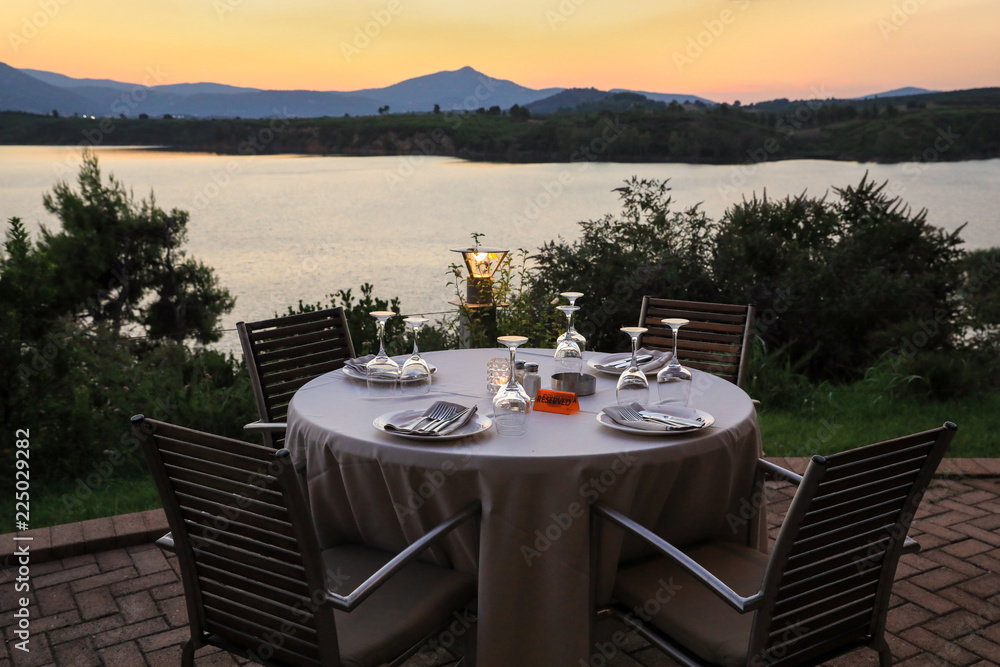 Romantic summer evening in the restaurant - table served for four persons with a sunset view at the lake Marathon, Greece.