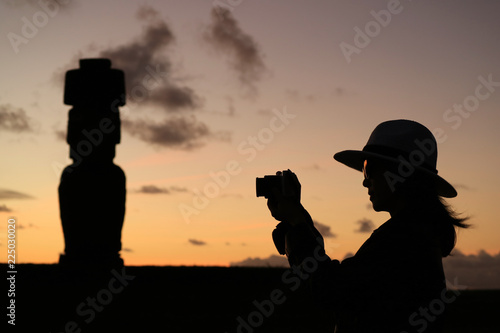 Silhouette of a female tourist taking pictures of the famous Moai statue at Ahu Tahai on Easter Island, Chile