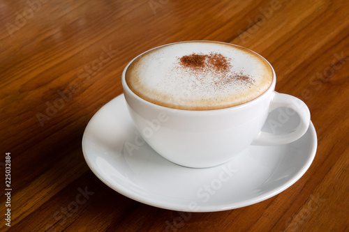 Hot coffee cappuccino latte in white ceramic cup on wooden table background
