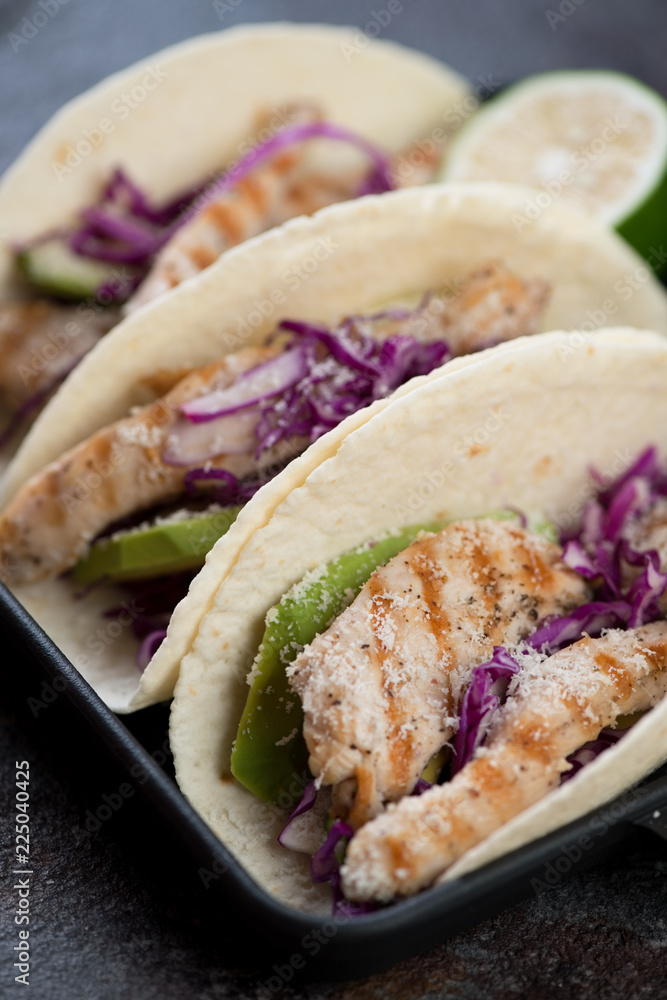 Close-up of tacos filled with grilled chicken fillet, red cabbage and avocado and topped with grated cheese, selective focus Close-up of tacos filled with grilled chicken fillet, red cabbage and avocado and topped with grated cheese, selective focus