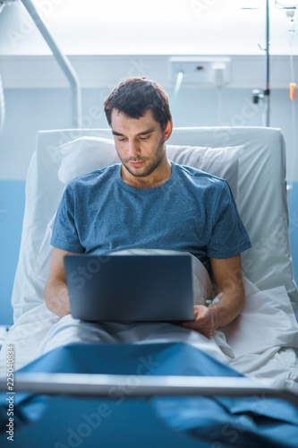 In the Hospital, Recovering Male Patient Uses Laptop while Lying on the Bed. Working even when Sick and in Hospital.