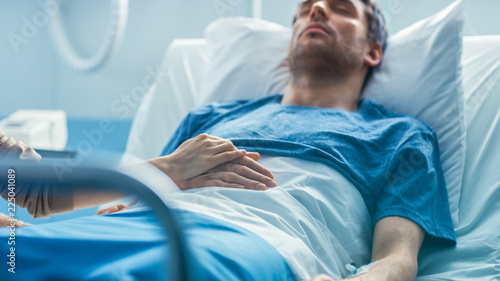 Photos In the Hospital Sick Man Lying on the Bed, His Visiting Wife Hopefully Sits Beside Him Holds His Hands and Hopes for Recovery