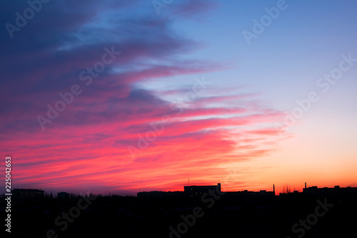 Red, pink and blue bright sunset over the city. City industrial landscape against the backdrop of the setting sun and clouds. Sunset with silhouette of city buildings.