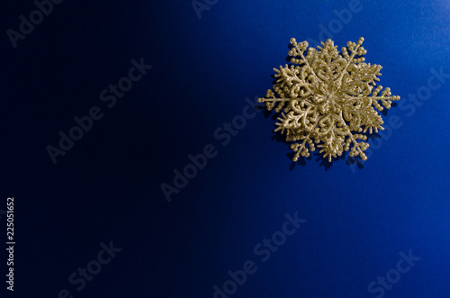 Close-up of a decorative golden snowflake on the up-right corner of a blue gradient background. Light from right