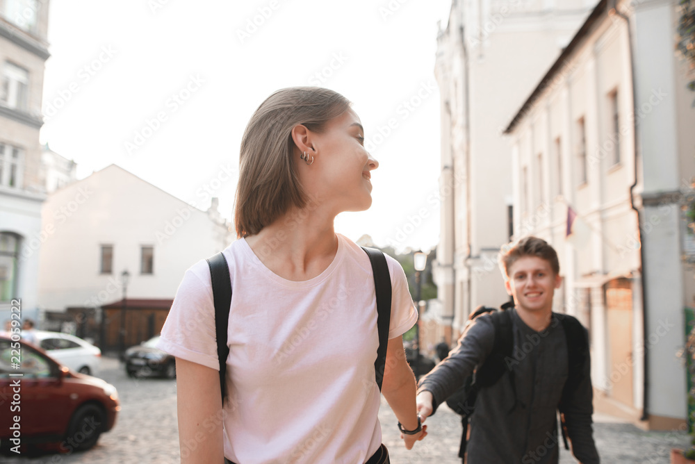 Attractive girl walking with her young man by the hand of a street in the background of the sunset. Follow me.