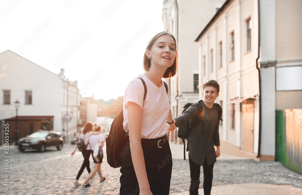 Obraz premium Attractive girl holds a young man by the hand and goes with him along the street of the old town on the background of the sunset. Happy man follows a girl on the background of the sunset. Follow me.