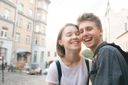 Smiling happy couple on the background of the sunset and old architecture. Beautiful guy and girl smiling at sunset and looking at the camera. Positive couple in love outdoor portrait.