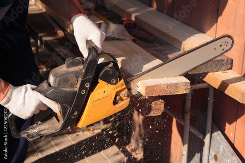 A carpenter cuts lumber with chainsaw, sawdust fly to side