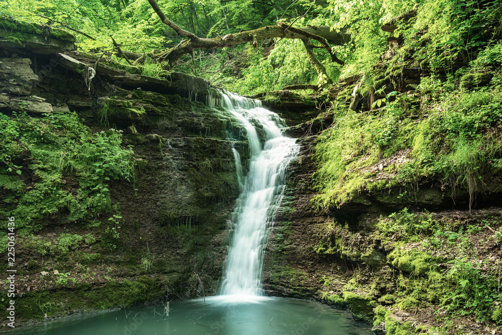 Beautiful mountain rainforest waterfall with fast flowing water and rocks, long exposure. Natural seasonal travel outdoor background in hipster vintage style