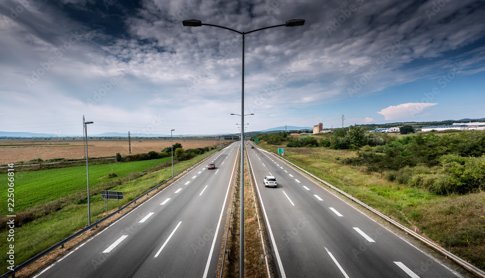 Highway Traffic on a straight road on a Cloudy Day through pastoral landscape