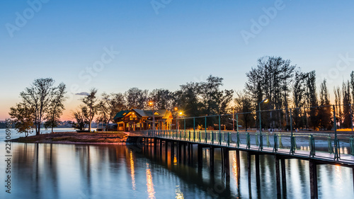 bridge leading to the island with wooden cottages illuminated by evening illumination. evening scene. © ROMAN