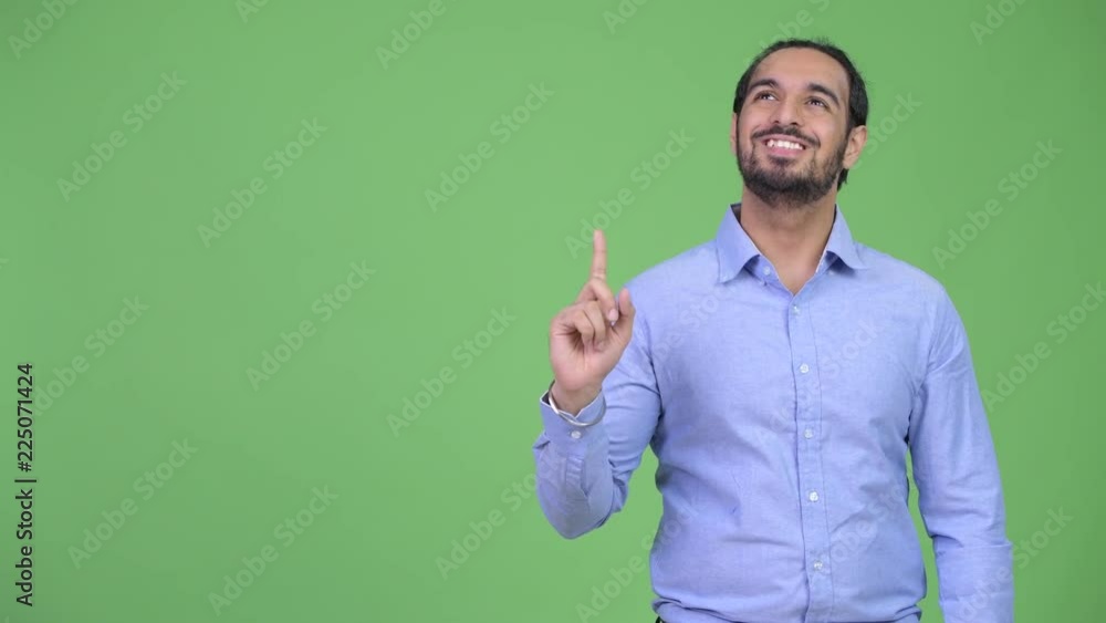 Young happy bearded Indian businessman thinking while pointing up Young happy bearded Indian businessman thinking while pointing up