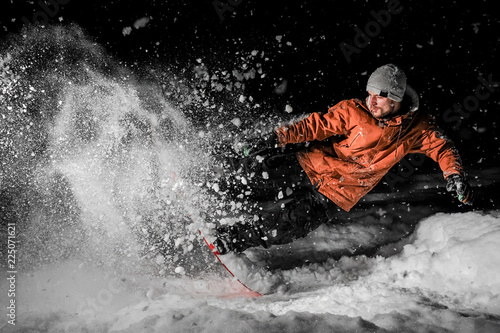 Young snowboarder in orange sportswear jumping on the board at night