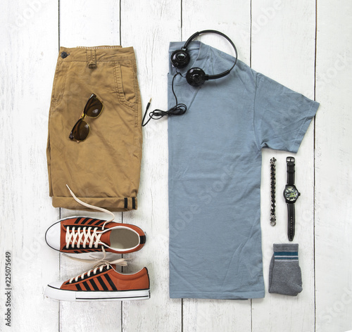 Fashionable concept, men’s clothes with sneakers, t shirt, yellow shorts, watch, sunglasses,sock, earphone and bracelet on white wooden background. pack shots, top view