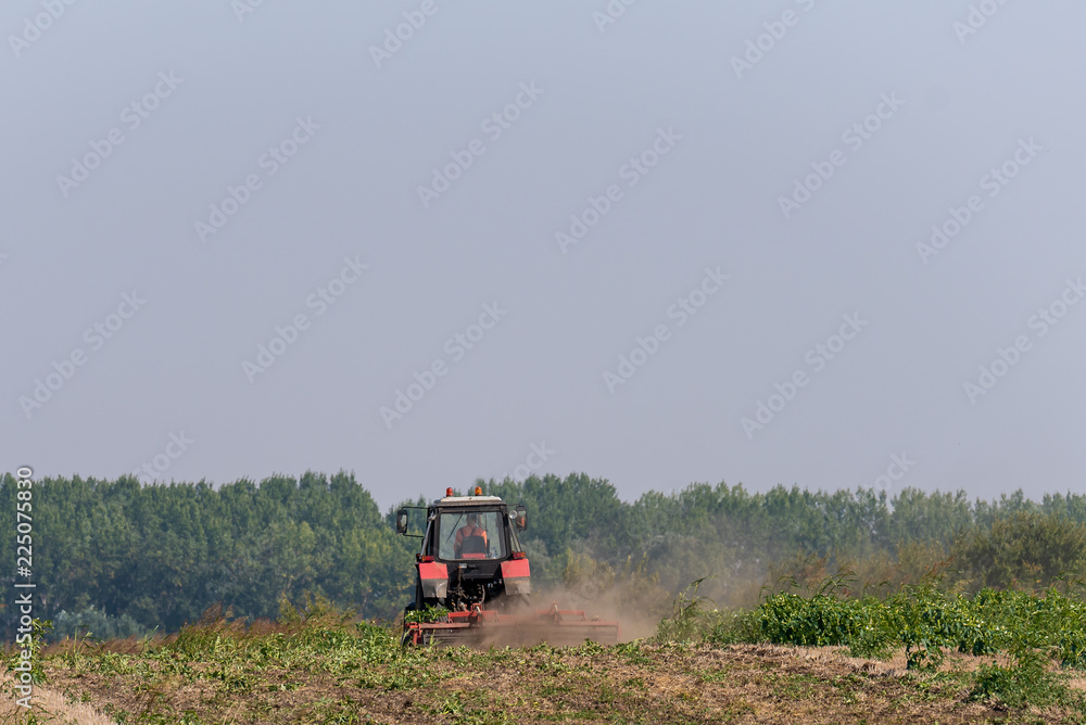 Fototapeta premium The red tractor works in the field in autumn
