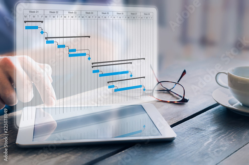 Obraz na płótnie Project manager updating progress and deliverables milestones schedule on gantt chart planning with digital tablet computer, professional planner in office w salonie