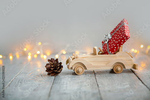Foto wooden car with gift on a wooden gray background and lights from the garland