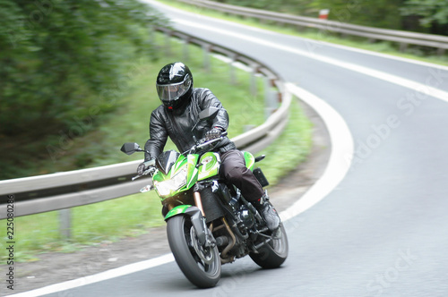The driver of a green, sports motorcycle, wearing a complete safety suit, goes into a bend at high speed. The beginning of the motorcycle season is open.