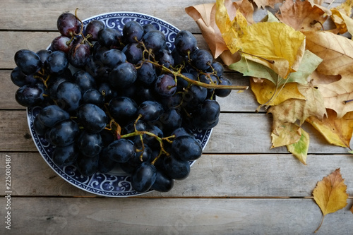 Bowl of grapes on a rustic wooden table decorated with autumn leaves 